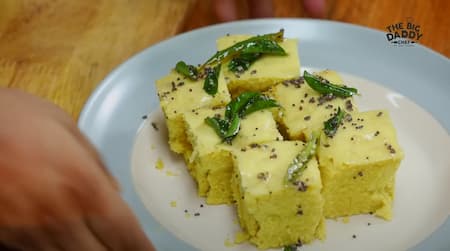 Garnishing Dhokla with chopped coriander leaves and grated coconut before serving.
