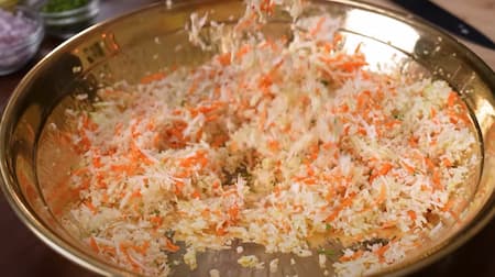 Grated carrot and cabbage, with chopped onions, green chilies, and coriander on a cutting board.