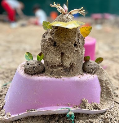 Imagem mostra bolo de areia sobre uma bacia cor de rosa.