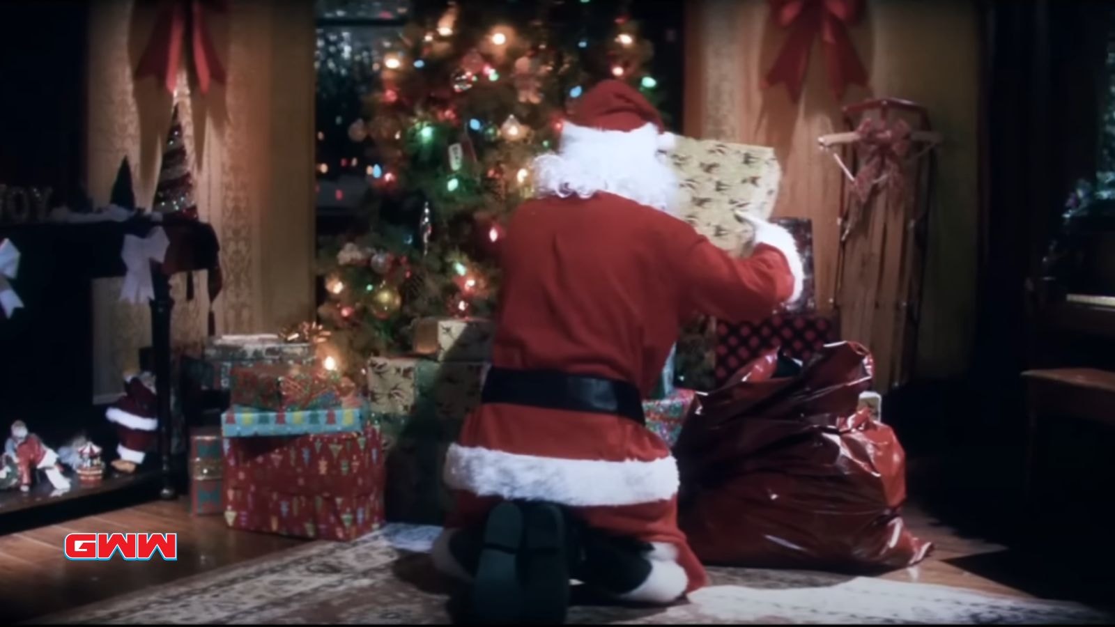 Santa placing presents under a decorated Christmas tree at night.