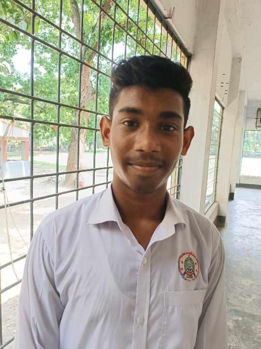 South Asian teen boy with short trimmed brown hair, clean cut, white collared school uniform shirt in a school hallways near windows open to the outside where there are trees. 