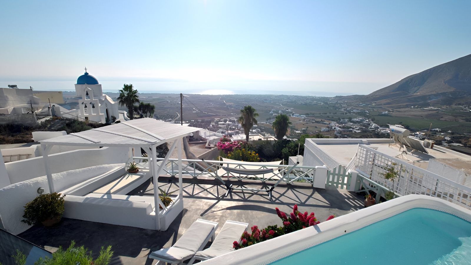 A pool of a vacation rental in Santorini with the views of the mountains and white-washed buildings. 