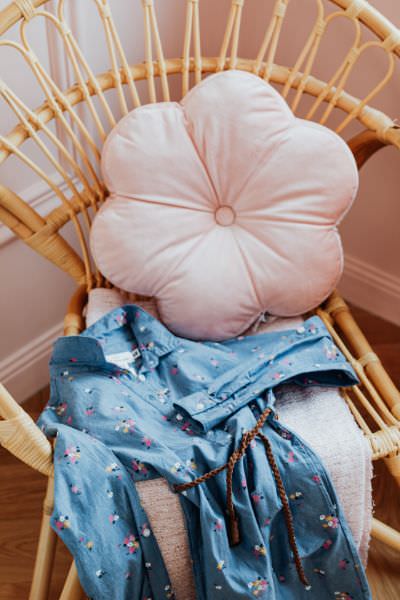 Ein Baumwollkleid aus Kinderstoff und ein Blumenkissen auf einem Korbstuhl