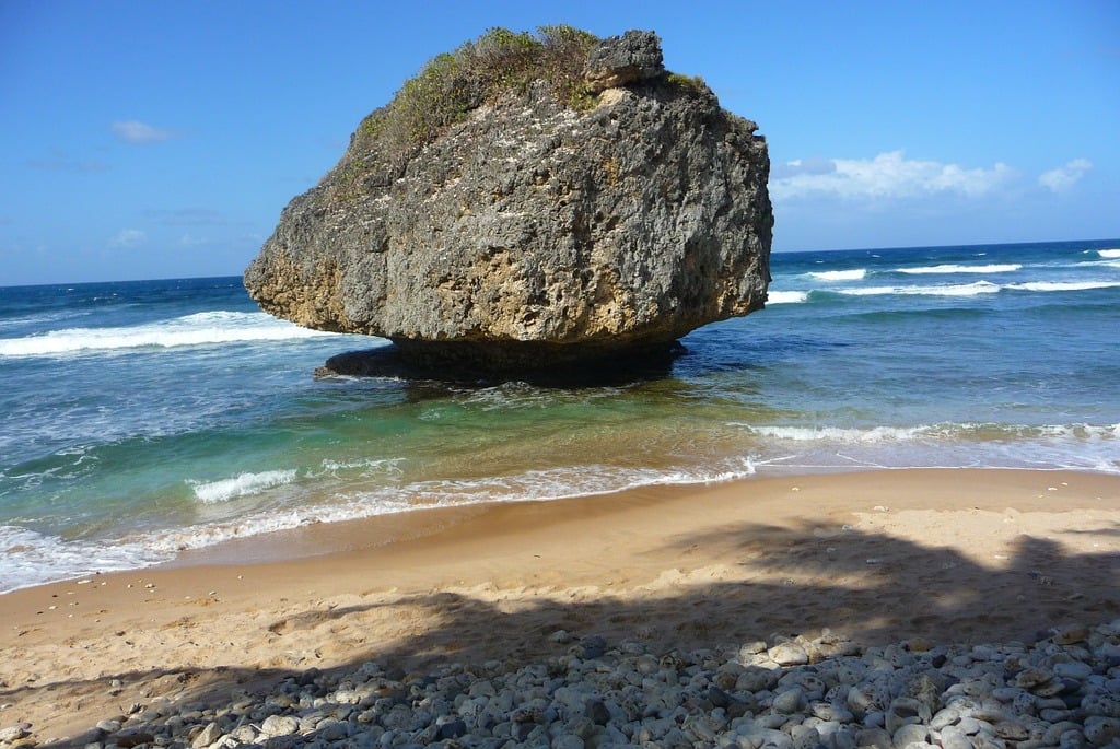 Sandy beach with clear water and a massive rock in the center of the water