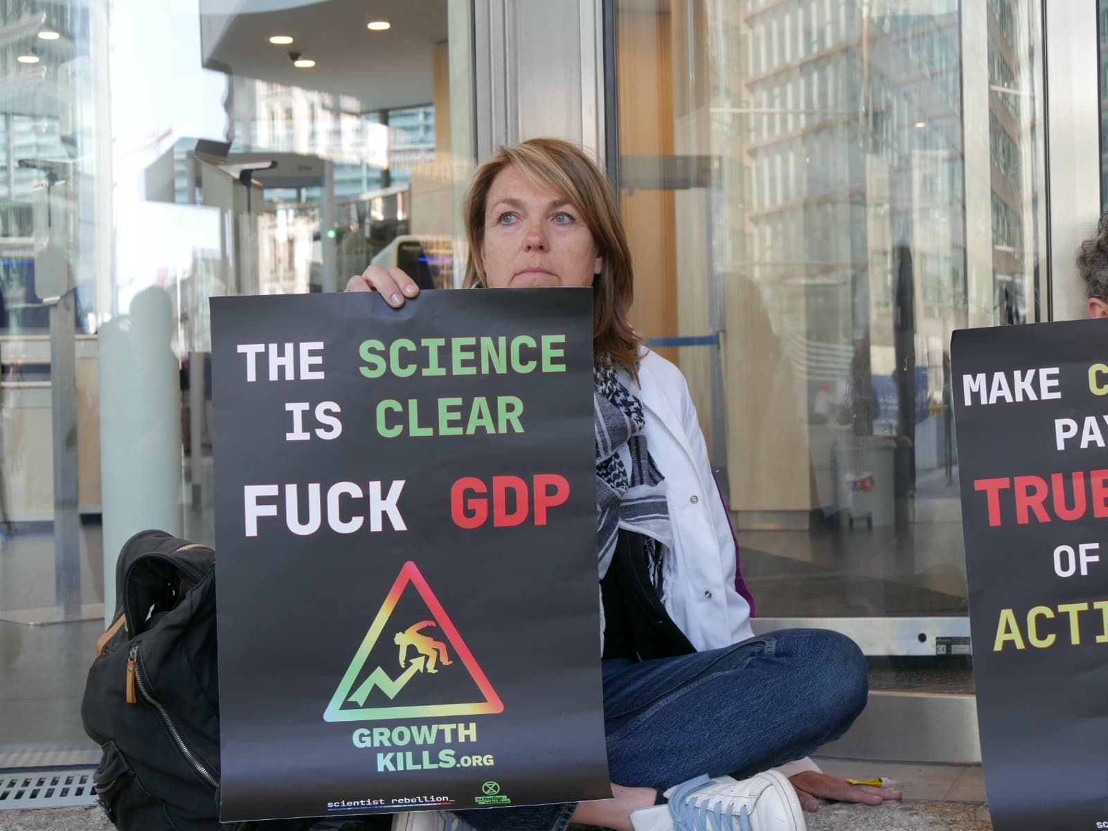 A woman kneels outside the EU Commission with an anti-GDP banner