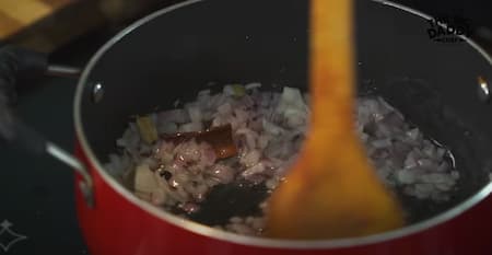 Onions sautéing in a pan with cumin seeds and ginger-garlic paste, forming the base for the masala.