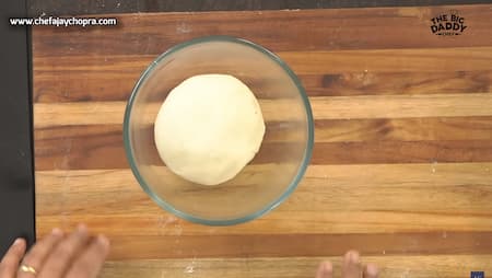 A bowl with frothy yeast mixture, flour, and a well in the center ready for kneading into pizza dough.