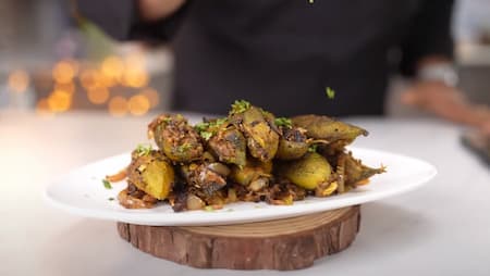 Adding tadka with sliced onions and spices to the cooked Bharva Karela.