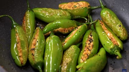 Stuffed chilies sautéing in a pan with mustard oil and kalonji.