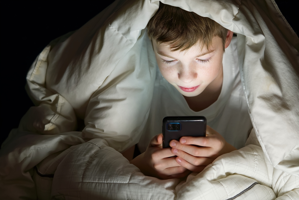 Young boy sitting in bed with his cell phone