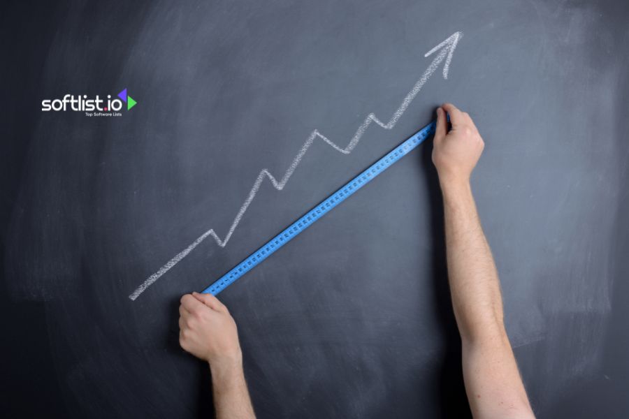 Hand drawing an upward trend line on a blackboard with a blue ruler.