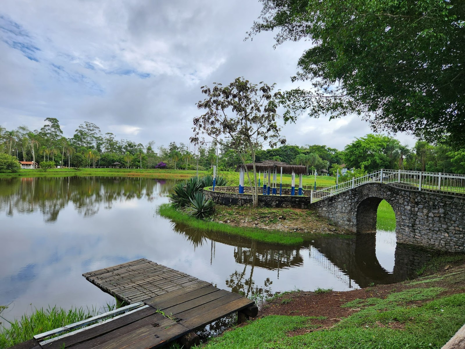 Lago de um parque com um pequeno deck e uma ponte que leva a uma pequena ilha.