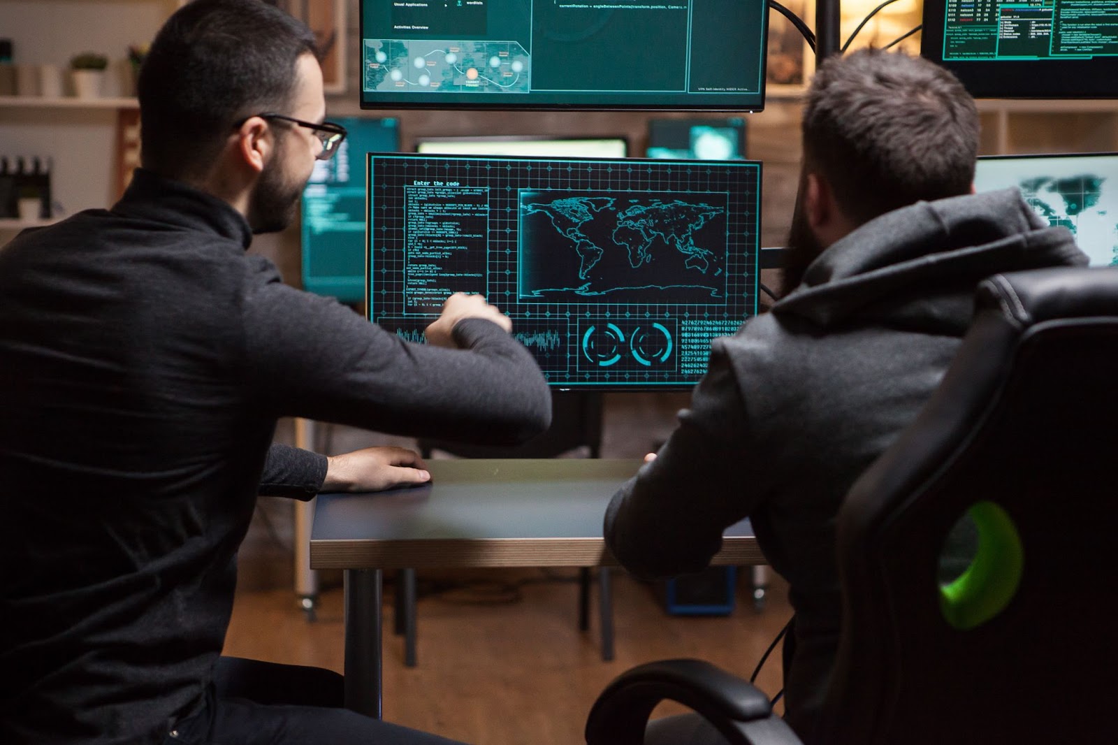 Two cybersecurity officers in black outfits are planning a cyber counterattack on their system, with several screens displaying data reflecting NDAA cybersecurity initiatives.