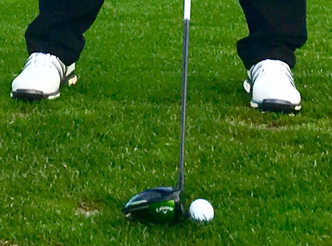 a golfers feet in a good stance ready to hit a driver off the tee box without a tee