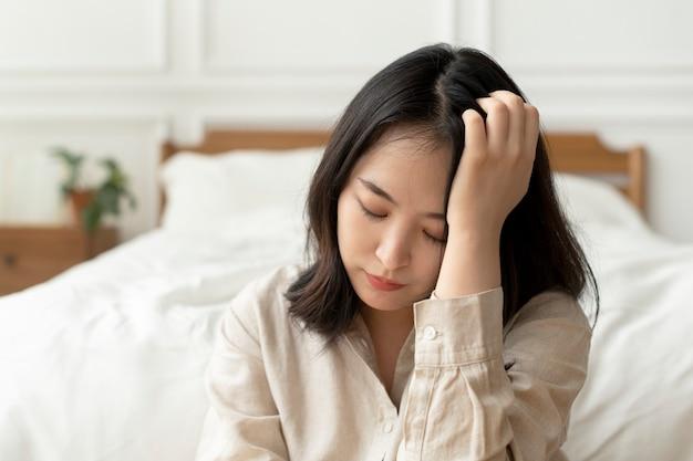 Free photo asian woman sitting sad by her bed