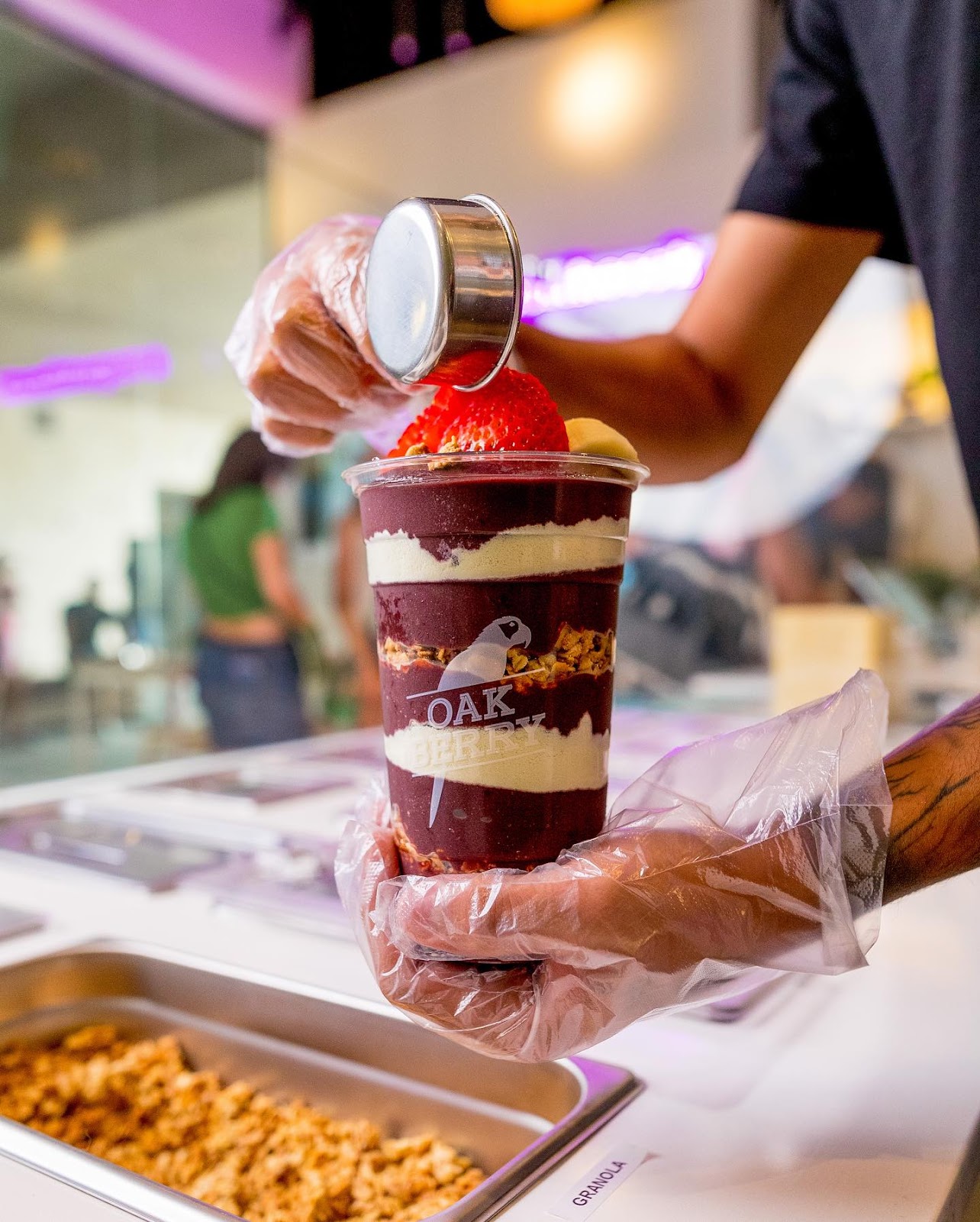 OAKBERRY layered açaí smoothie, employee tops drink with fresh fruit