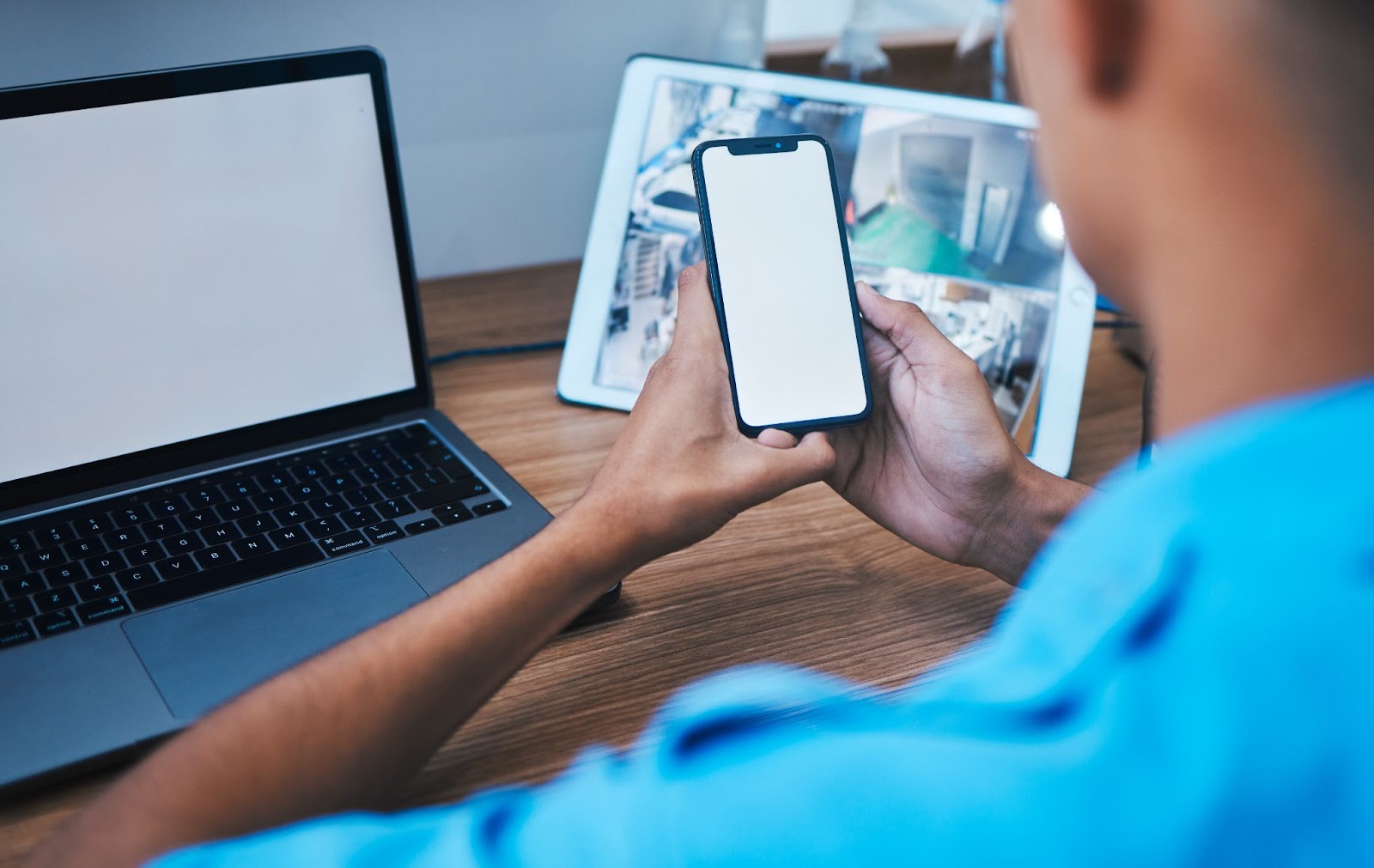 A male employee in a blue uniform stands with his back facing the camera, testing their new workforce management solution with a phone, laptop, and mockup space.