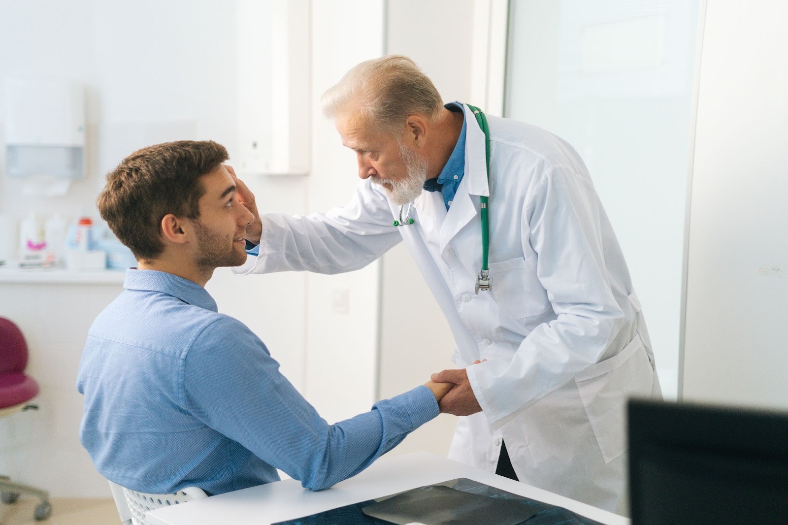 A male ophthalmologist examining a male patient's left eye to diagnose his condition.
