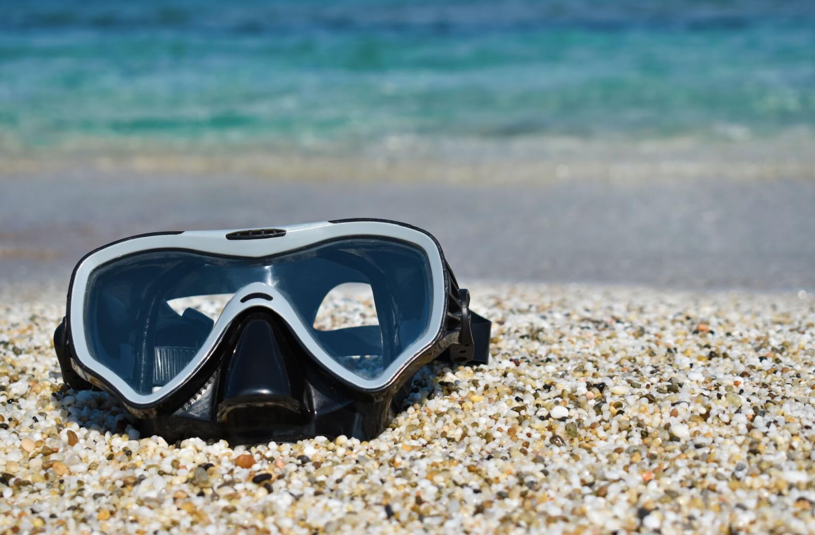 A close-up of a  scuba diving mask on a sandy shore.