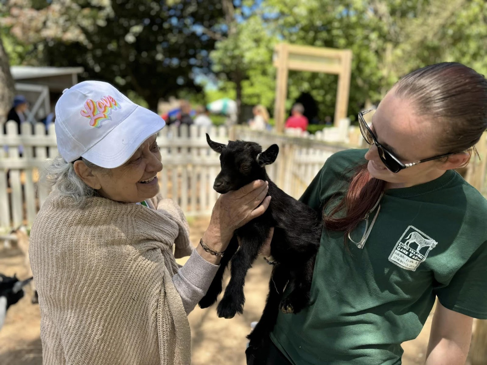 A Village Walk resident petting a baby goat with a Long Island Game Farm employee