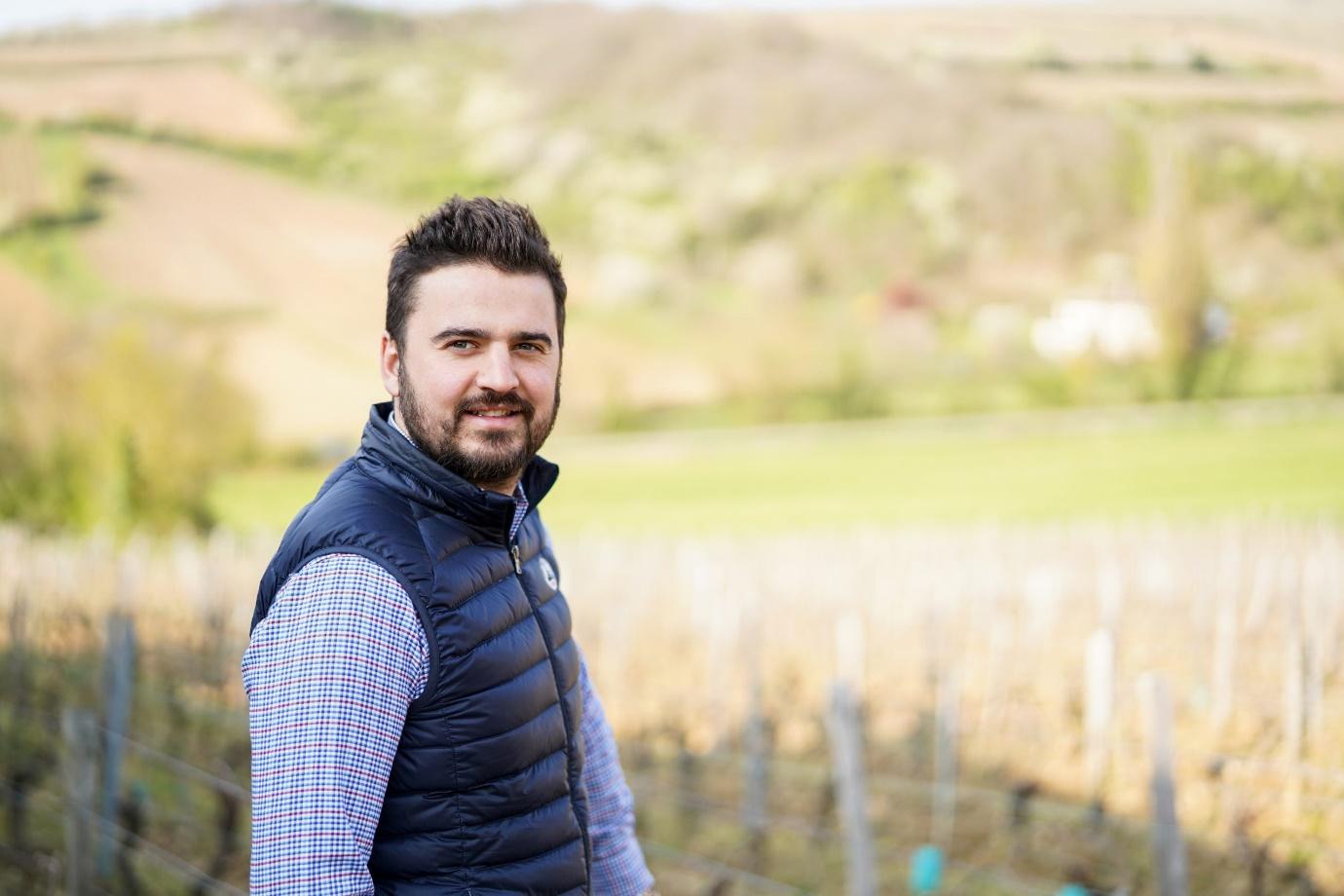 A person standing in front of a vineyard

Description automatically generated