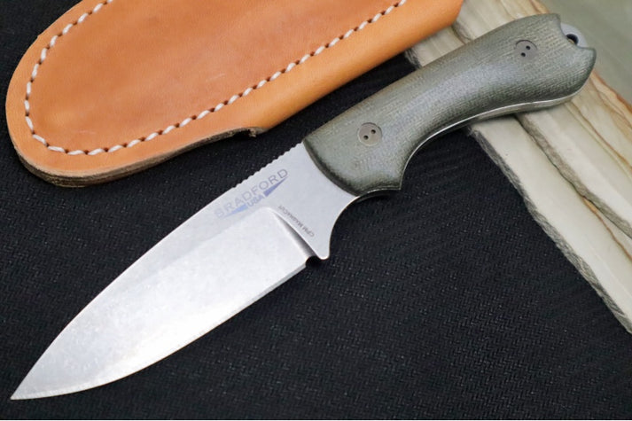 An image showcasing the Bradford Knives Guardian 3.2S with OD green Micarta handle on a black and wood background. To the left of the knife is a tan leather sheath.