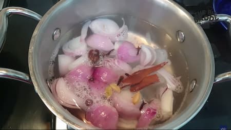 Boiling onions with spices for a smooth paste in Chicken Kali Mirch recipe.