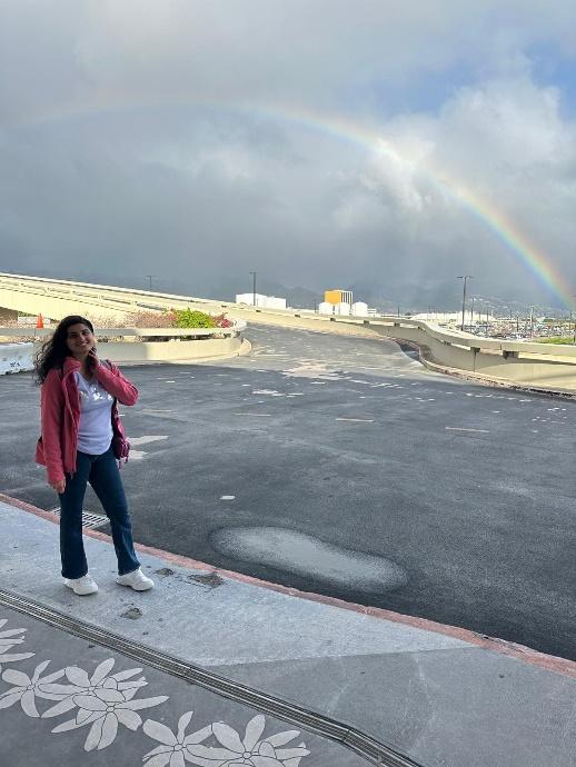 A person standing on a sidewalk with a rainbow in the background

Description automatically generated