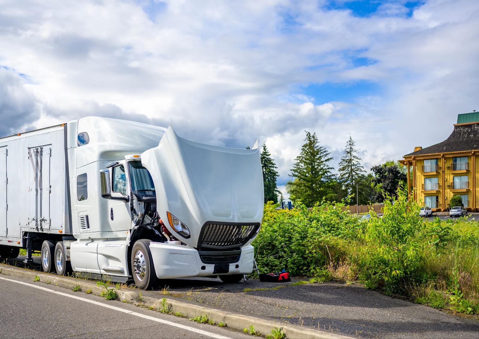 A broken-down semi truck sits on the side of the road with its hood up