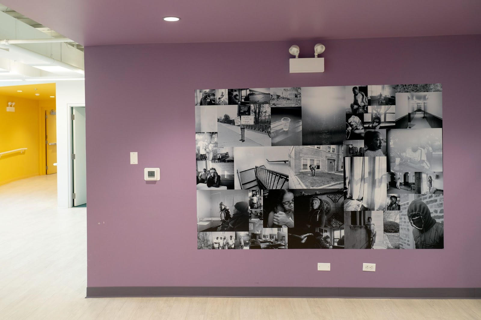 Installation view: A rectangular collage of Sasha Phyars-Burgess’ work against a purple wall at BUILD Chicago in Austin. The collage includes several portraits of individuals and couples, as well as still scenes of hallways and objects like light shining on a plastic cup of water. All of the photographs are in black-and-white. Courtesy of Villa Albertine.