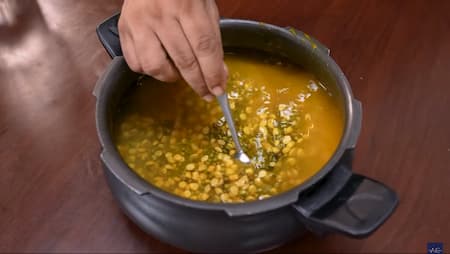 Soaked green moong dal and chana dal being boiled in a pressure cooker with turmeric and salt.