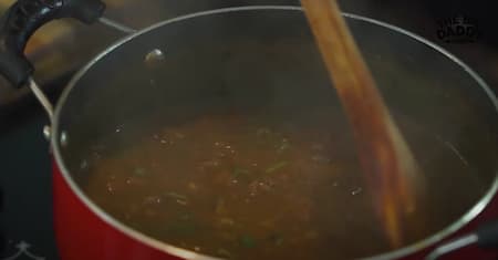 Cooked rajma being mixed with the masala in the pan, allowing flavors to meld together.
