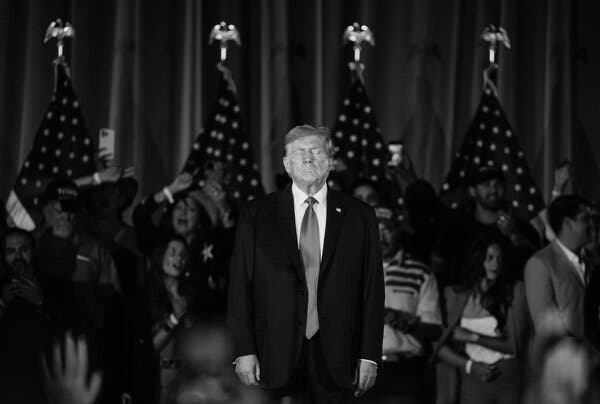 With his eyes closed, Donald Trump stands in front of a group of well-wishers snapping photos.