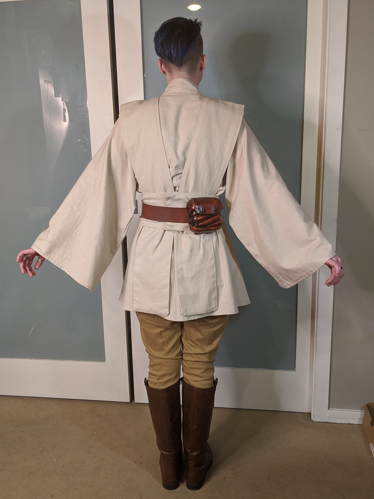 Image description: A person in a Jedi costume, facing backwards, with their arms extended down and to the sides /end description