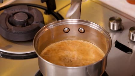 Adding sugar to the saucepan with tea, milk, and spices, stirring it in.