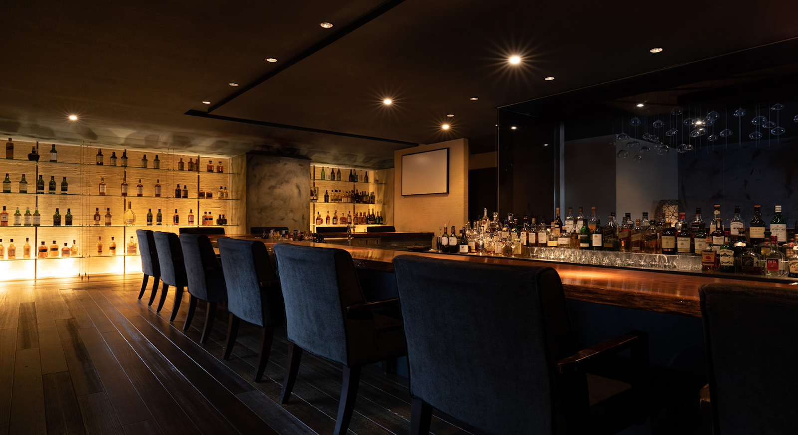 image of the bars interior with blue elegant chairs on the counter, an assortment of bottles in the background