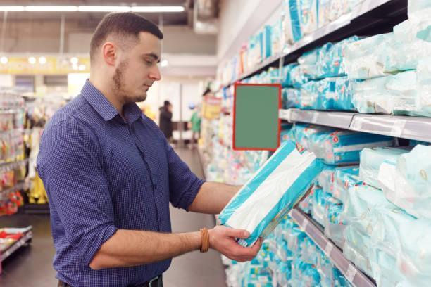 man with diaper pack in supermarket reading product information man with diaper pack in supermarket reading product information. adult diapers stock pictures, royalty-free photos & images