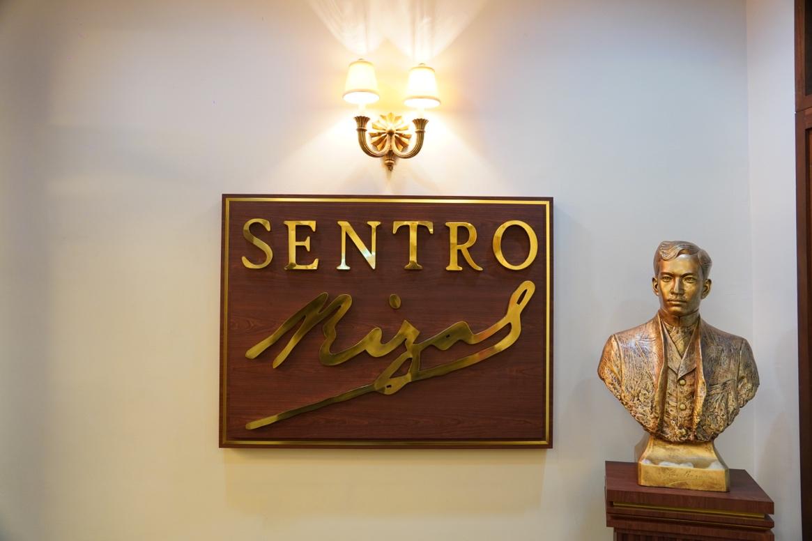 A statue of a person in front of a signDescription automatically generated