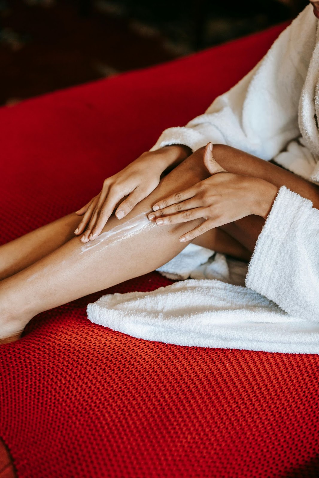 Woman sitting on red couch applying luxurious moisturizer to her legs