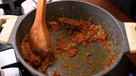 Ginger-garlic paste and green chilies being added to a golden brown onion masala mixture in a pan.