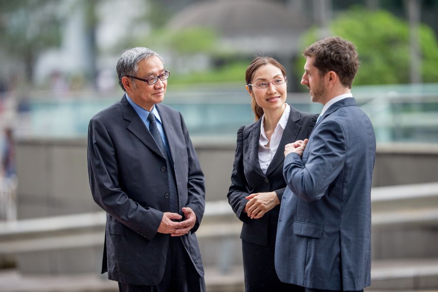 Three business people having a conversation outdoors in a corporate setting.