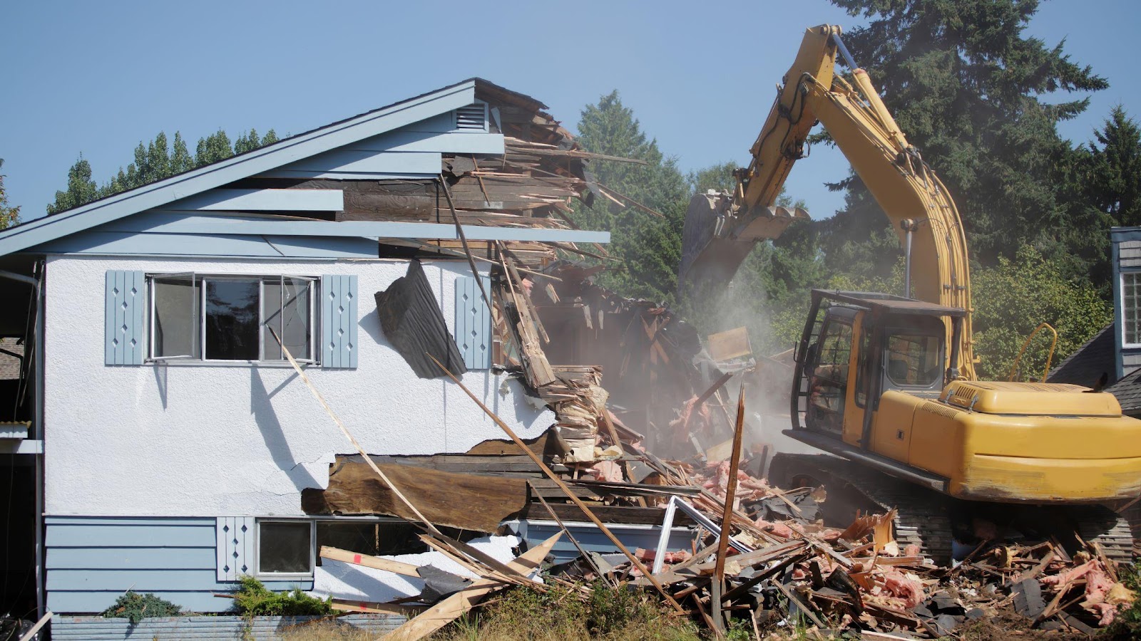 An excavator demolishing a damaged house, illustrating the drastic step of home demolition as part of post-disaster recovery, emphasising the critical signs that lead to such a decision.