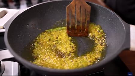 Cumin seeds spluttering in hot mustard oil along with garlic, green chilies, and ginger in a pan.