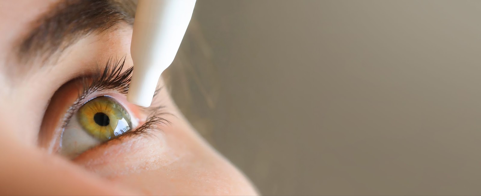 A close-up image of a woman applying eye drops to her left eye.