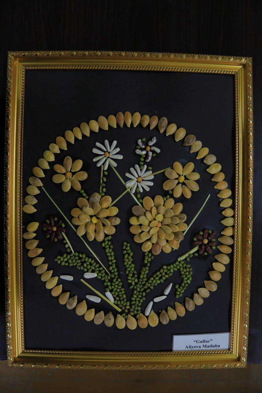 Image of a bouquet of flowers surrounded by a tan circle. All made of seeds of varying colors. 