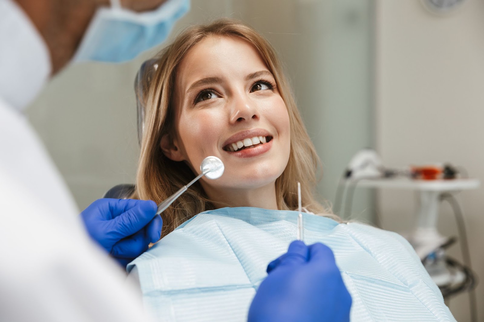 A woman in a dental chair smiling at her dentist while being inspected for a cavity.