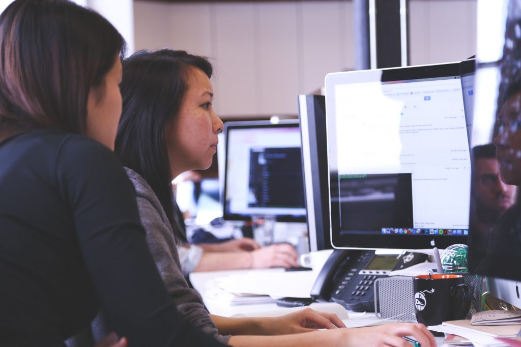 two women sitting at a computer - one is helping the other in business