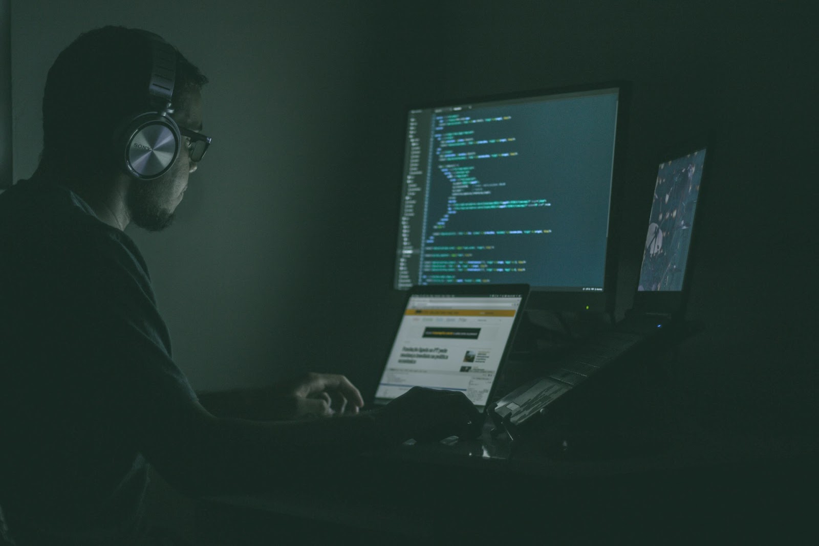 A man in headphones sitting at a computer with a screen showing code.