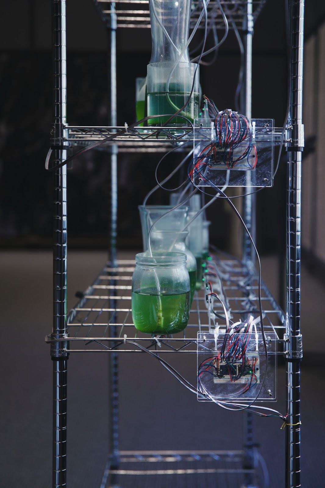 side view of a storage shelf. a breadboard is affixed to a piece of acrylic, attached to the side of the shelf. there are several red and blue wires attached to the breadboard