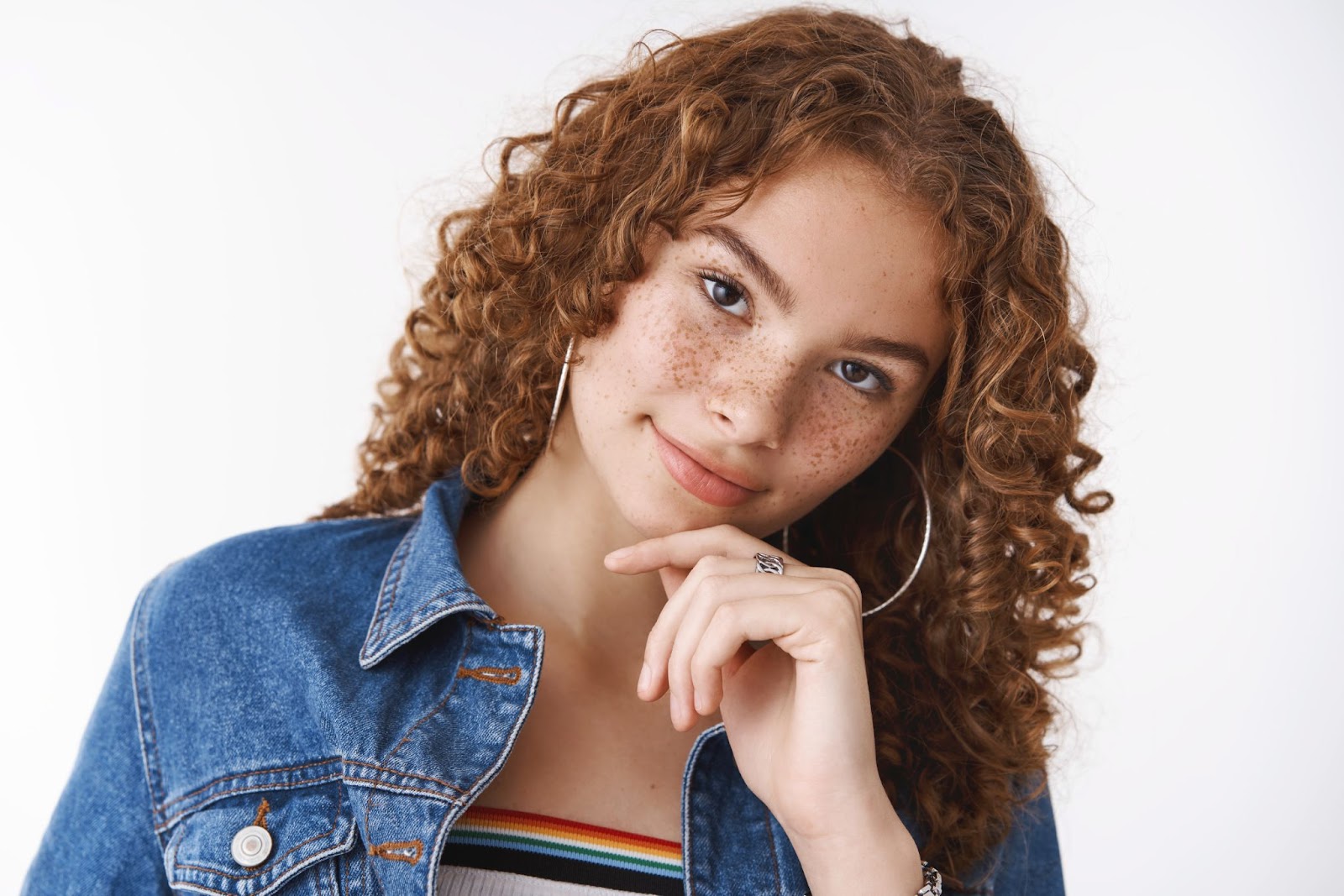 Mulher com cabelo cacheado ruivo acobreado sob um fundo branco. 